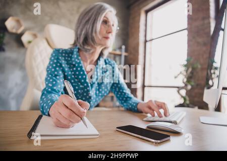 Photo d'une vieille femme sérieuse écrire dans un cahier travail femme d'affaires travail focalisé travail assis bureau à l'intérieur dans le bureau Banque D'Images