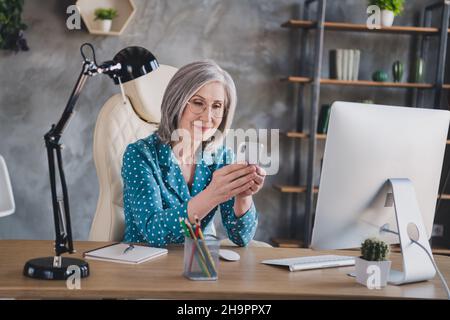 Photo de calme grave vieille jolie femme look téléphone écrire message affaires à l'intérieur dans le bureau lieu de travail Banque D'Images