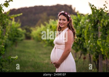 Femme enceinte tenant son ventre.Portrait d'une jeune femme souriante qui attend son bébé dans un vignoble Banque D'Images