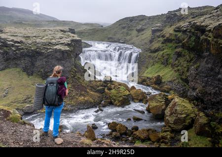 Randonneur avec grand sac à dos de randonnée en face de la cascade, paysage au sentier de randonnée de Fimmvoerouhal, Islande du Sud, Islande Banque D'Images