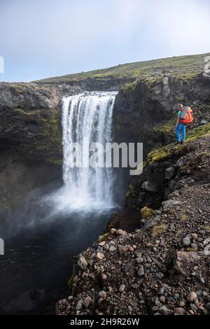 Randonneur avec grand sac à dos de randonnée en face de la cascade, paysage au sentier de randonnée de Fimmvoerouhal, Islande du Sud, Islande Banque D'Images