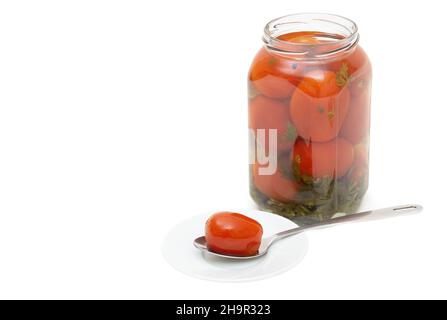 La tomate marinée dans une cuillère sur une soucoupe blanche près du pot de tomates prune salées isolées sur blanc Banque D'Images