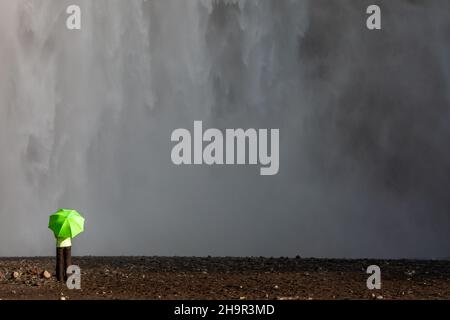 Femme randonneur explorer avec un parapluie vert bras levés debout devant une cascade.Environnement, réchauffement de la planète, changement climatique concept. Banque D'Images