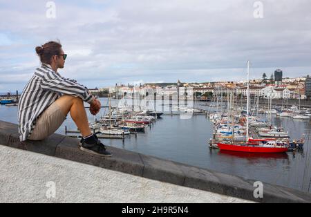 Jeune homme assis sur la promenade dans le port de plaisance de Ponta Delgada, île de Sao Miguel, Açores, Portugal Banque D'Images