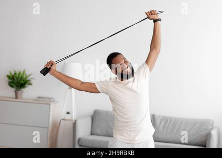 Joyeux millennium afro-américain barbu gars faisant des exercices avec corde à sauter dans le salon Banque D'Images