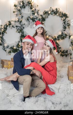 Photo du nouvel an d'une famille mixte heureuse avec une jolie fille.Mère, père et fille portent des chapeaux de Noël rouges.Tout le monde sourit Banque D'Images