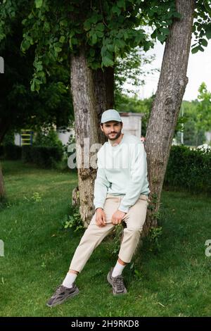 homme barbu sur toute la longueur en chapeau, penché sur les troncs d'arbre dans le parc Banque D'Images