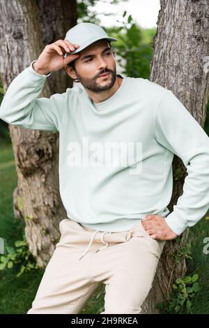 homme barbu qui règle la casquette et se tient près des troncs d'arbre dans le parc Banque D'Images