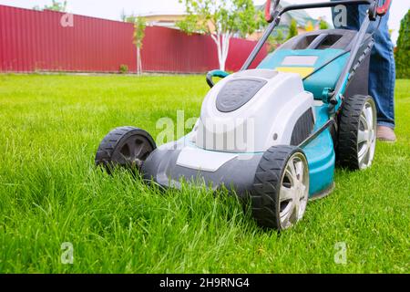 Une tondeuse, un gros plan.Un travailleur coupe de l'herbe dans la cour arrière-cour par temps ensoleillé. Banque D'Images