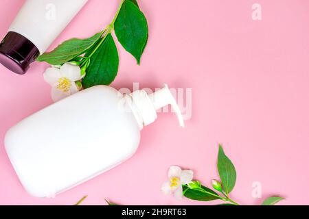 Vue de dessus du contenant à cosmétiques en plastique blanc pour la crème hydratante comme un modèle avec des fleurs de jasmin fraîches et lumineuses sur fond rose avec espace de copie. Banque D'Images