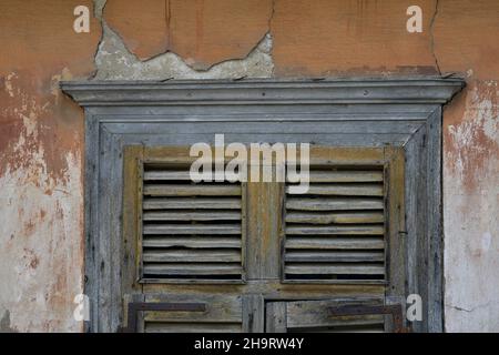 Ancienne fenêtre de maison néoclassique avec des volets en bois gris altérés contre un mur de stuc vénitien fade à Nafplio, Grèce. Banque D'Images