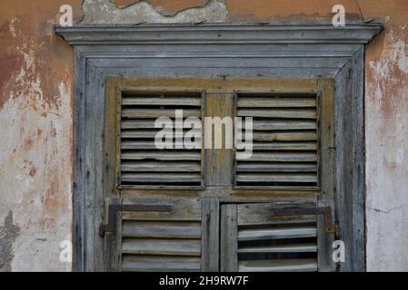 Ancienne maison néoclassique ancienne fenêtre avec des volets en bois gris altérés contre un mur en stuc vénitien fade à Nafplio, Grèce. Banque D'Images
