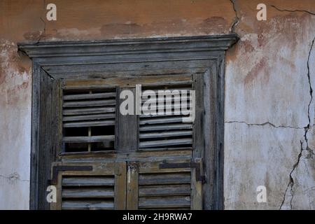 Ancienne maison néoclassique ancienne fenêtre avec des volets en bois gris altérés contre un mur en stuc vénitien fade à Nafplio, Grèce. Banque D'Images