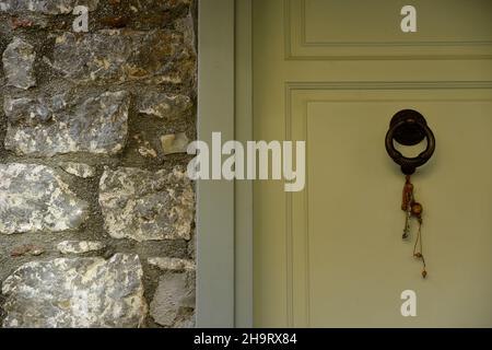 Ancienne maison traditionnelle, porte d'entrée en bois jaune de maïs avec un ancien knocker en laiton et une perle de charme chanceux contre un mur en pierre fait à la main en Grèce Banque D'Images