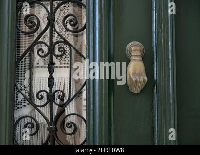 Ancienne maison néoclassique porte en bois vert cyprès avec grilles en fer artisanales, rideaux en dentelle et un ancien knocker en laiton à Nafplio, Grèce. Banque D'Images