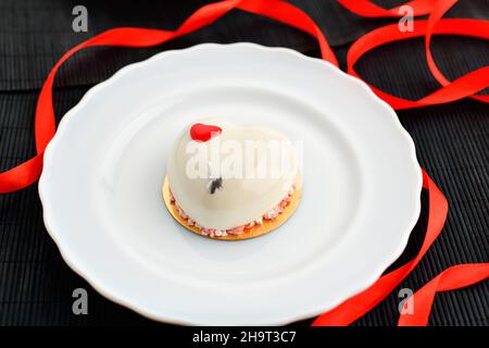 Un gâteau en forme de coeur.Un gâteau de mousse en forme de coeur sur une assiette sur fond noir avec un ruban rouge.Saint Valentin. Banque D'Images