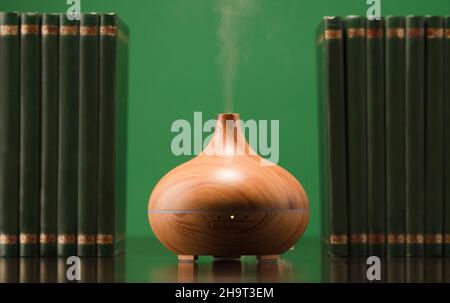 Évier aromatique, huiles essentielles sur la table avec des livres, surface vert clair avec réflexion.Arrière-plan vert. Banque D'Images