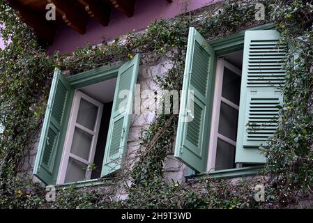 Façade traditionnelle de maison rurale avec volets de fenêtre en bois vert menthe contre un mur rose pâle à Nafplio, Grèce. Banque D'Images