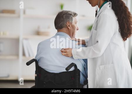 Femme médecin utilisant le stéthoscope sur un homme plus âgé en fauteuil roulant à la maison Banque D'Images