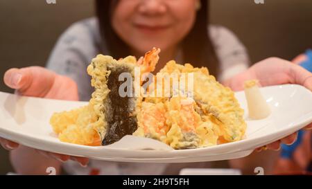 Une femme tenant une assiette de tempura de crevettes appétissantes avec un sourire heureux. Banque D'Images