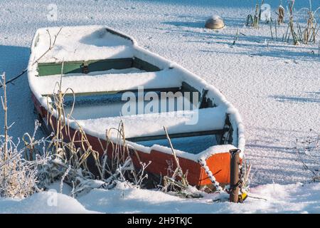 Bateau en bois coloré empilé sur un lac gelé recouvert de neige sur la plage avec des roseaux Banque D'Images