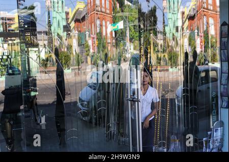 '16.12.2013, Myanmar, , Yangon - Une femme se tient derrière une porte vitrée d'un magasin dans le centre de l'ancienne capitale, reflétant une scène de rue.0SL1312 Banque D'Images