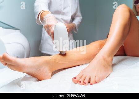 Épilation au laser et cosmétologie dans un salon de beauté.Épilation au laser, soins de la peau.Maître méconnaissable fait l'enlèvement de cheveux au laser sur les jambes de la femme. Banque D'Images