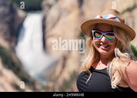 Belle jeune femme blonde portant un chapeau fedora pose au Grand Canyon de la chute d'eau du parc national de Yellowstone Banque D'Images