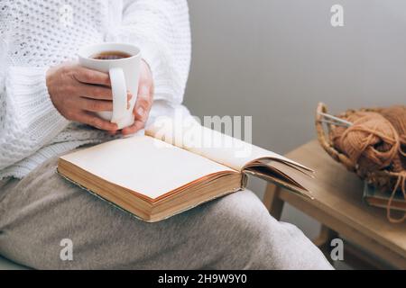 Une femme d'âge moyen est assise dans un fauteuil confortable à la maison avec une tasse de thé et lit un livre.La vie quotidienne, les passe-temps et les loisirs des personnes d'âge moyen Banque D'Images