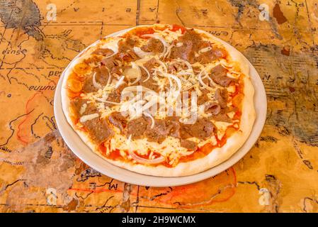 Pizza fraîchement préparée avec des ingrédients et de la viande de kebab ou de shawarma avec du fromage, des poivrons et beaucoup d'oignons et cuits dans un four à pierre. Banque D'Images