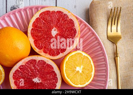 Délicieux pamplemousses et oranges pour le petit déjeuner avec café et argenterie dorée sur une assiette rose. Banque D'Images