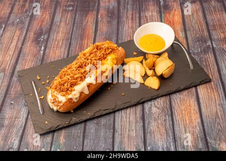 Hot dog avec oignon croustillant, cheddar et moutarde avec quartiers de pommes de terre sur plaque d'ardoise noire Banque D'Images