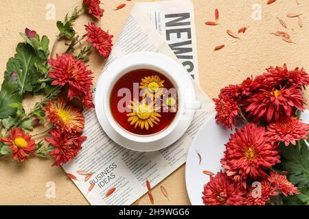 Composition avec tasse de thé, journal et fleurs de chrysanthème sur fond de couleur, gros plan Banque D'Images