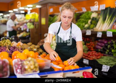 Une jeune fille de quinze ans qui travaille à temps partiel comme une vendeuse stagiaire met des mandarines Banque D'Images