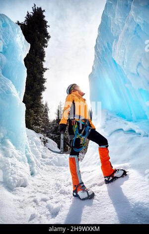 Femme grimpeur près d'une chute d'eau gelée dans un casque avec hache glacée dans une veste orange dans les montagnes.Sport alpinisme et alpinisme concept. Banque D'Images