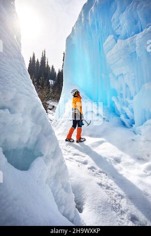 Femme grimpeur près d'une chute d'eau gelée dans un casque avec hache glacée dans une veste orange dans les montagnes.Sport alpinisme et alpinisme concept Banque D'Images