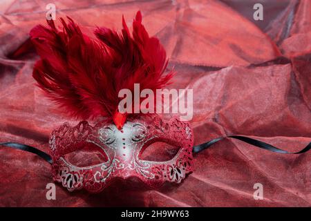 Carnival masque vénitien couleur rouge avec paillettes et plumes décoration sur fond textile rouge.Déguise traditionnelle féminine au festival, masq. Mardi gras Banque D'Images