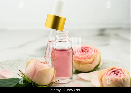 une bouteille ouverte d'huile de rose et une pipette remplie de cosmétiques pour le rajeunissement et le soin du visage sur fond de marbre Banque D'Images