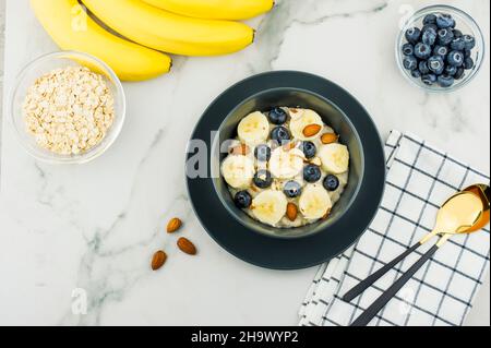 porridge de flocons d'avoine maison sain dans un bol sombre avec des tranches de banane mûre et des bleuets. amandes pour améliorer le vkua. vue du dessus. table en marbre Banque D'Images