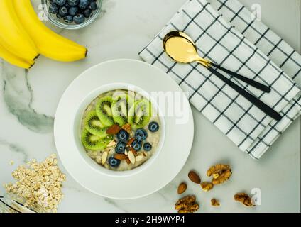 petit déjeuner sain. porridge de flocons d'avoine avec kiwi, bleuets et noix dans un bol blanc sur un comptoir en marbre. flocons d'avoine, bananes mûres. vue du haut Banque D'Images