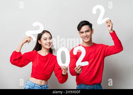 Jeune couple asiatique souriant montrant le numéro 2022 dans un fond gris clair isolé pour le nouveau concept d'année Banque D'Images