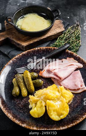 Raclette de fromage fondu avec pomme de terre bouillie et jambon sur une assiette rustique, repas suisse.Arrière-plan noir.Vue de dessus Banque D'Images