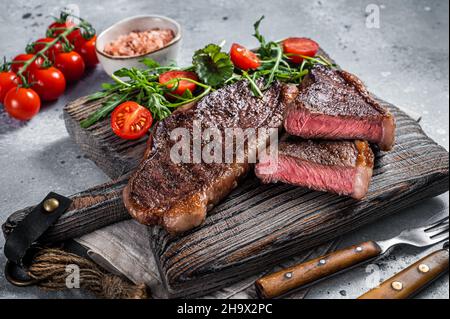 Steak de viande de bœuf rôti au chapeau ou au sirloin supérieur sur une planche de bois avec salade.Arrière-plan gris.Vue de dessus Banque D'Images