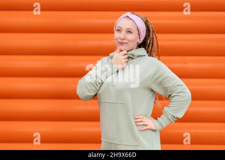 Portrait d'une jeune femme pensive avec des dreadlocks se posant contre un mur en bois orange.Le concept de psychologie et de problème. Banque D'Images