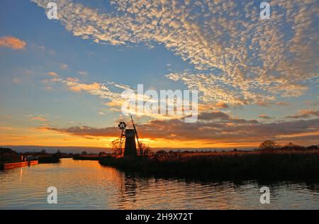 Un paysage avec grand ciel et moulin à vent rétroéclairé par un coucher de soleil en automne par la rivière Ant sur les Norfolk Broads près de Ludham, Norfolk, Angleterre, Royaume-Uni. Banque D'Images