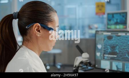 Spécialiste en biologie travaillant avec l'ordinateur pour examiner l'animation de l'adn en laboratoire.Microbiologiste avec lunettes de protection utilisant des équipements de laboratoire pour travailler sur des expériences scientifiques pour l'innovation. Banque D'Images