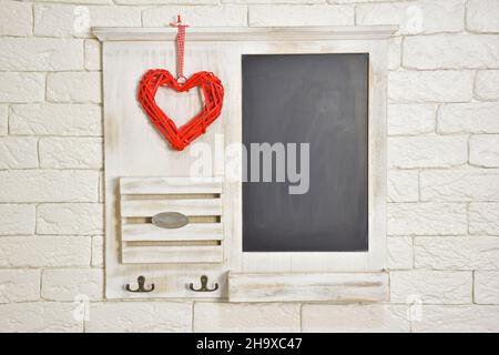 Un tableau pour inscriptions et un coeur rouge stylisé en osier naturel sont suspendus sur le fond d'un mur de briques claires.Il y a un endroit Banque D'Images