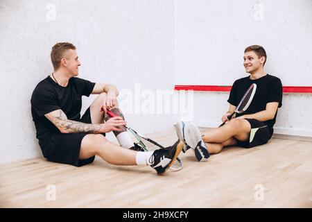 Portrait complet de deux garçons sportifs, joueurs de squash se reposant après un jeu d'équipe actif et productif Banque D'Images