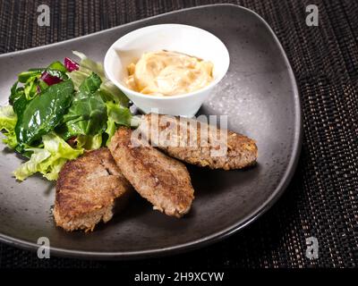 Côtelettes de viande sautées servies avec une sauce crémeuse et une salade verte fraîche sur une assiette sombre Banque D'Images