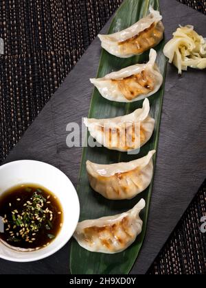 Boulettes de gyoza japonaises traditionnelles sur plaque d'ardoise noire, servies avec une sauce soja. Photo verticale Banque D'Images